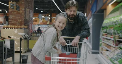 Slow Motion Portrait of Young Man Father Pushing Shopping Cart with Little Girl Daughter in