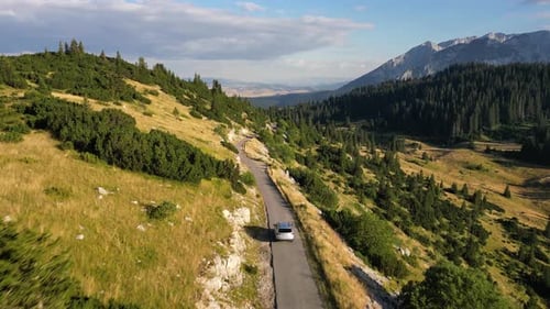 The car drives along a beautiful mountain road, around the forest and epic mountains. Aerial view.
