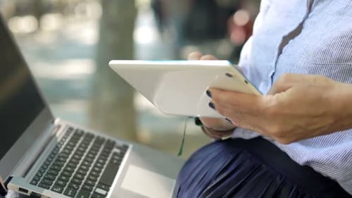 Elegant businesswoman works with tablet and laptop on bench in the city