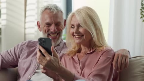 Senior Couple Laughing Together at Smartphone Indoors