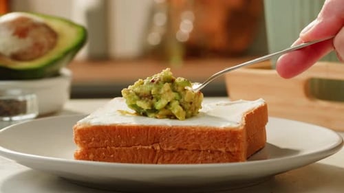 Person Spreads Avocado on Toast with Cream Cheese