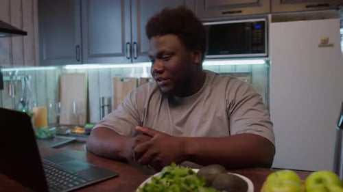 Young Adult Using Laptop with Produce on Table