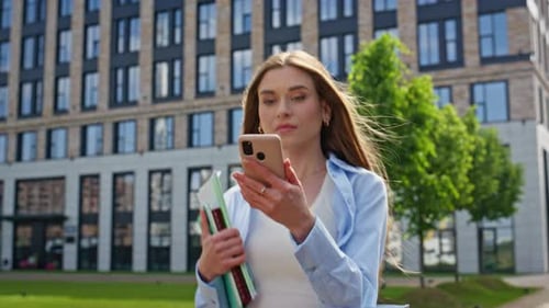 Excited Woman Looking Cellphone Walking Sunny Street with Books Closeup