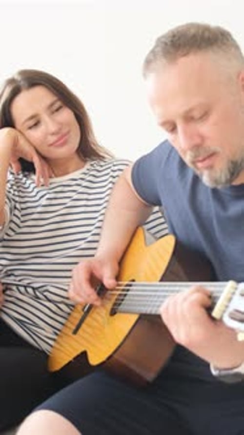 Man Plays Guitar as Woman Listens Indoors