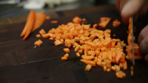 Young chef expertly chopping fresh carrots on a cutting board in restaurant