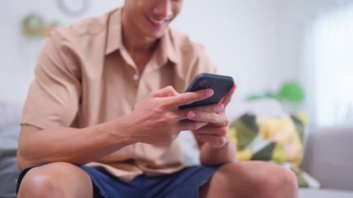 Young Man Using Smartphone Smiling on Sofa Indoors
