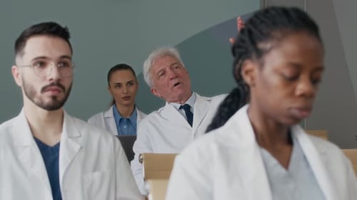 Senior Male Physician Asking Question at Group Seminar in Conference Hall