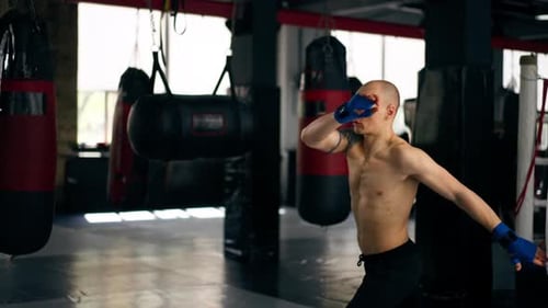 in a Boxing Fight Club Bald Young Boxer with Tattoos in Blue Bandages Trains a Kick Before a Fight