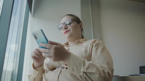 Woman in business attire using smartphone while sitting at a table in an office environment