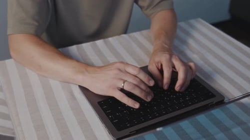 Top View of Male Hands Typing on Laptop Keyboard at Table