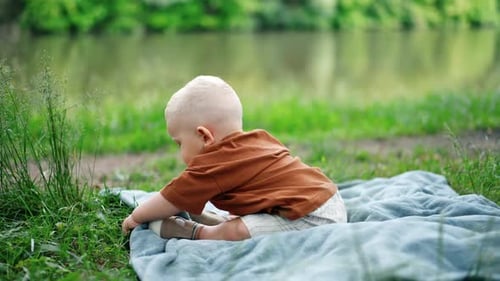 Ein
entzückender kleiner Junge sitzt auf dem Plaid im Gras. Das Kleinkind berührt interessiert das Gras
.
