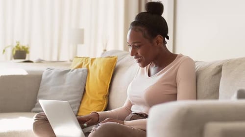 Young Happy African American Woman Reading News Online on Laptop and Smiling Typing Post in Social
