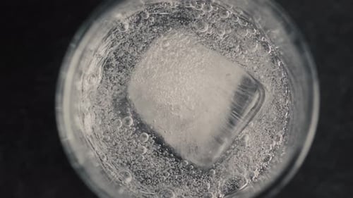 Ice cube melts slowly in glass of water
