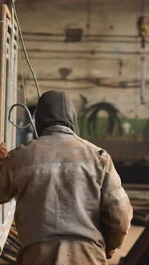 Laborer in Uniform Carries Metal Frame of Pipes in Workshop