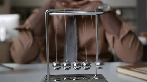 African American Man Pensively Looking at Newtons Cradle at Office Desk