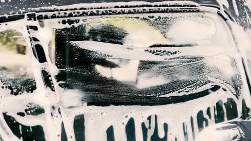 Close up of a male washing a car wearing a black gloves with shampoo and sponge
