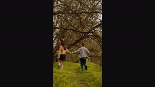 A young couple holding hands run through the forest, embodying an active lifestyle and tourism. Spor