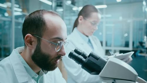 Scientists Working in Lab Analyzing Data Under Microscope