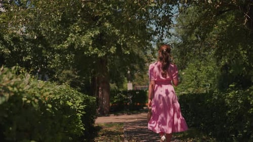 Sunlit Pathway Filled with Greenery Pink Dress Sways Along Quiet Garden Trail Lady in Pink Strolls