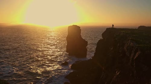 Seascape at Stone Cliffs at Sunset a Man Stands on Top of a Cliff and Takes Photos