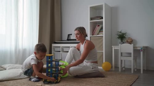 Mother and Her Son Playing Together with a Toy Garage Set on the Floor at Home