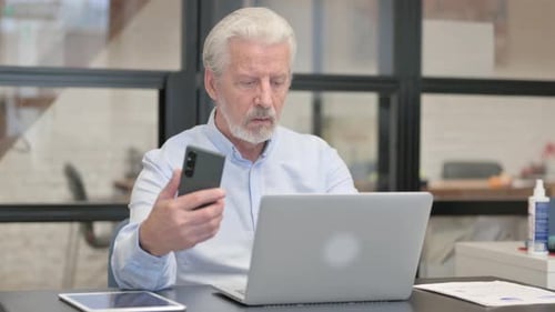 Senior Man Uses Smartphone at Office Desk