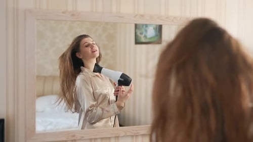 Young Woman Dries Hair in Front of Mirror