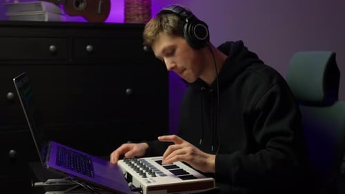 Young music producer creating beats on a MIDI keyboard, focused in a home studio with headphones,