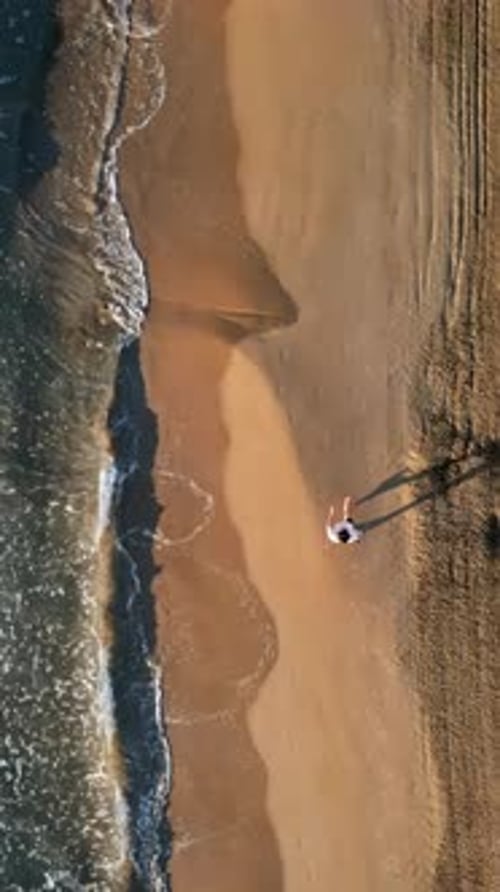Man walking on the beach with waves hitting the shore in Alicante, Spain. Vertical