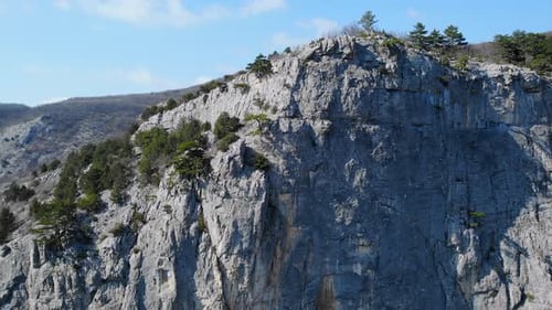 Felsige Klippe mit Bäumen vor blauem Himmel Media
