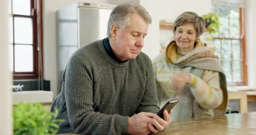 Senior Couple Sharing Smartphone Together in Kitchen