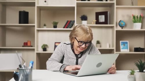 une femme plus âgée à lunettes commande la livraison de nourriture en ligne assise derrière son ordinateur portable et le coursier
