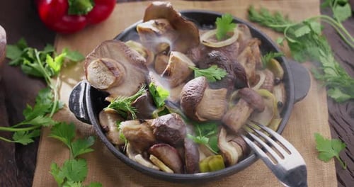 Frying pan with fried porcini mushrooms stands on a vintage wooden table and emits steam.