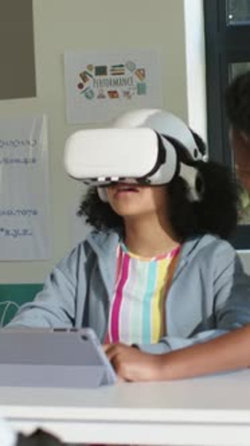 VR activating student wearing headset shifting head and reacting while classmate assisting learning