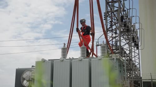 Uma construção civil está amarrando as cordas penduradas em um guindaste nos cantos de um transformador, então