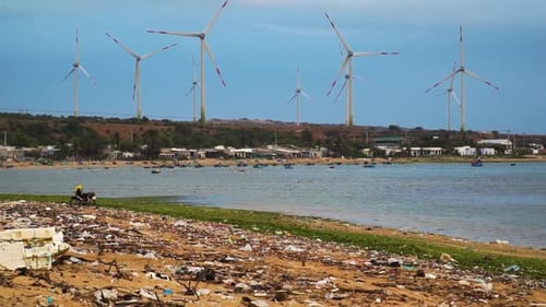 Rotating blades of clean And Renewable Wind Power Farm in background and polluted beach shore with p
