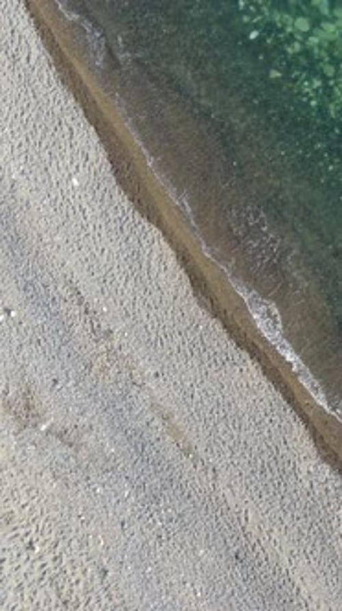 Aerial Vertical View of Beach with Wave Caressing Shore Sun Glare Small Waves on the Water Surface