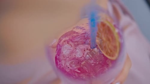 Hand einer jungen Frau, die mit einem Strohhalm einen Cocktail in einem Glas umrührt Nahaufnahme
