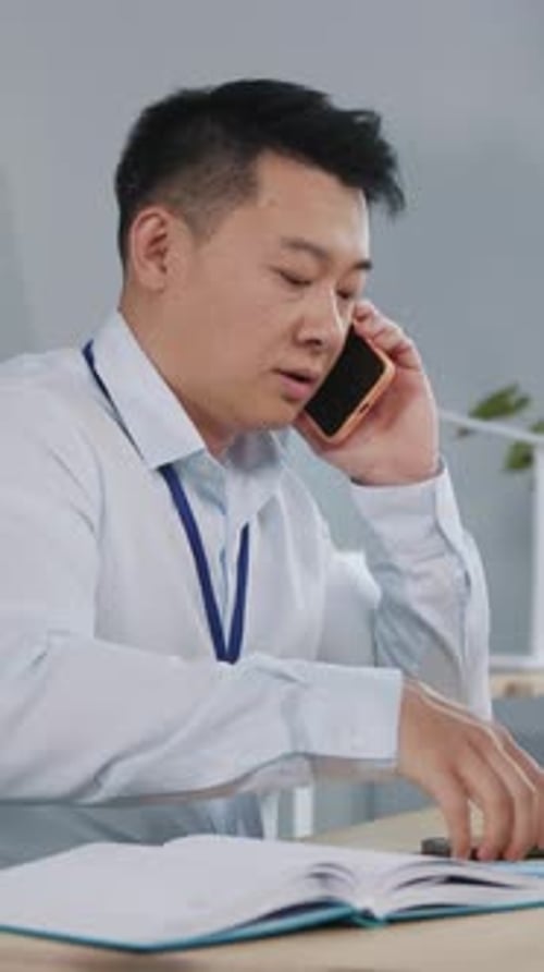 Man Sits at Desk, Using Two Phones at Once