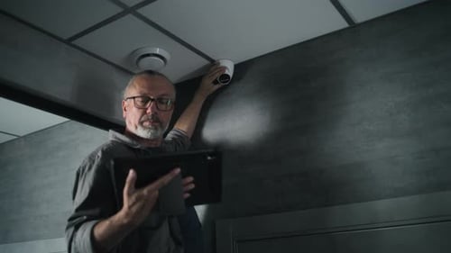 Male Installer Adjusts Angle of CCTV Camera in Office Sets Up It Using Tablet Computer