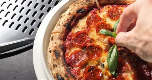 Hand Places Fresh Basil on Pepperoni Pizza