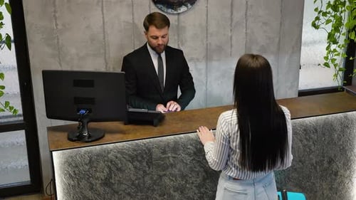 Hotel Receptionist Greeting Guest and Checking Her in