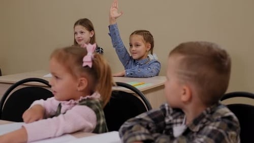 Group of Children is Sitting at a School Desk a Girl Raises Her Hands to Answer