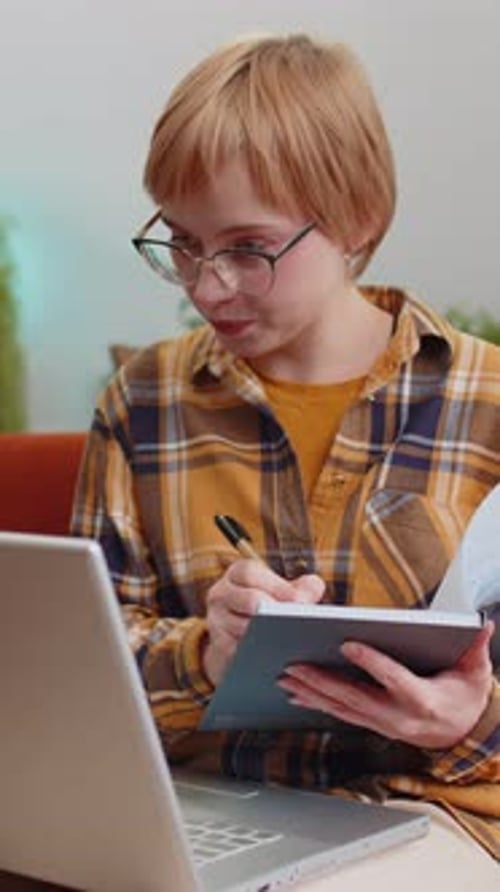 Woman Writes Notes Near Laptop In Cozy Home