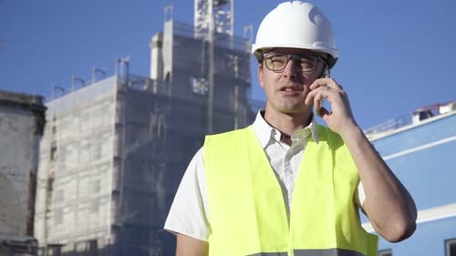 At the construction site, a young engineer wearing glasses and a white helmet is having a conversati