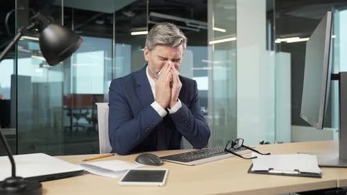 Man in Suit Sitting at Office Desk with Cold