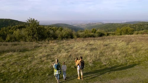 Aerial view of a smiling family of four enjoying a hike through a meadow on a hill.
