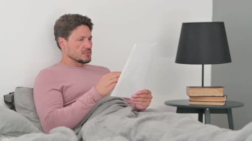 Man Reads Document in Bed, Gets Excited