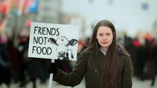Une femme tient une bannière Animal Friend Not Food avec une vache lors d'une manifestation végétalienne
