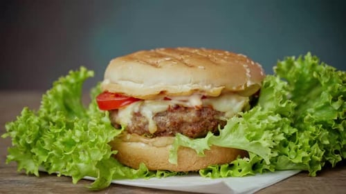 A Tasty Burger Lies on a Wooden Table against a green background. Close up